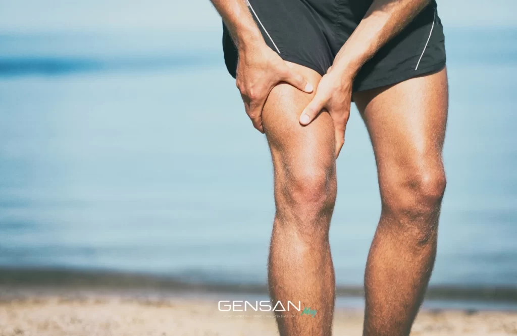 uomo in spiaggia si tocca una gamba a causa dei crampi muscolari